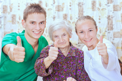 male and female caregiver with senior woman thumbs up and smiling