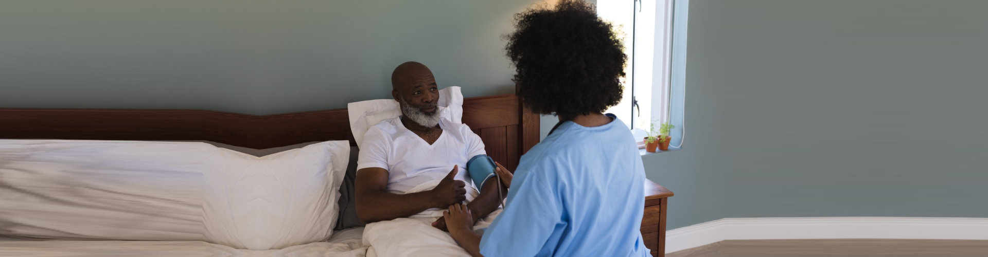 female nurse measuring blood pressure of senior man lying in the bed